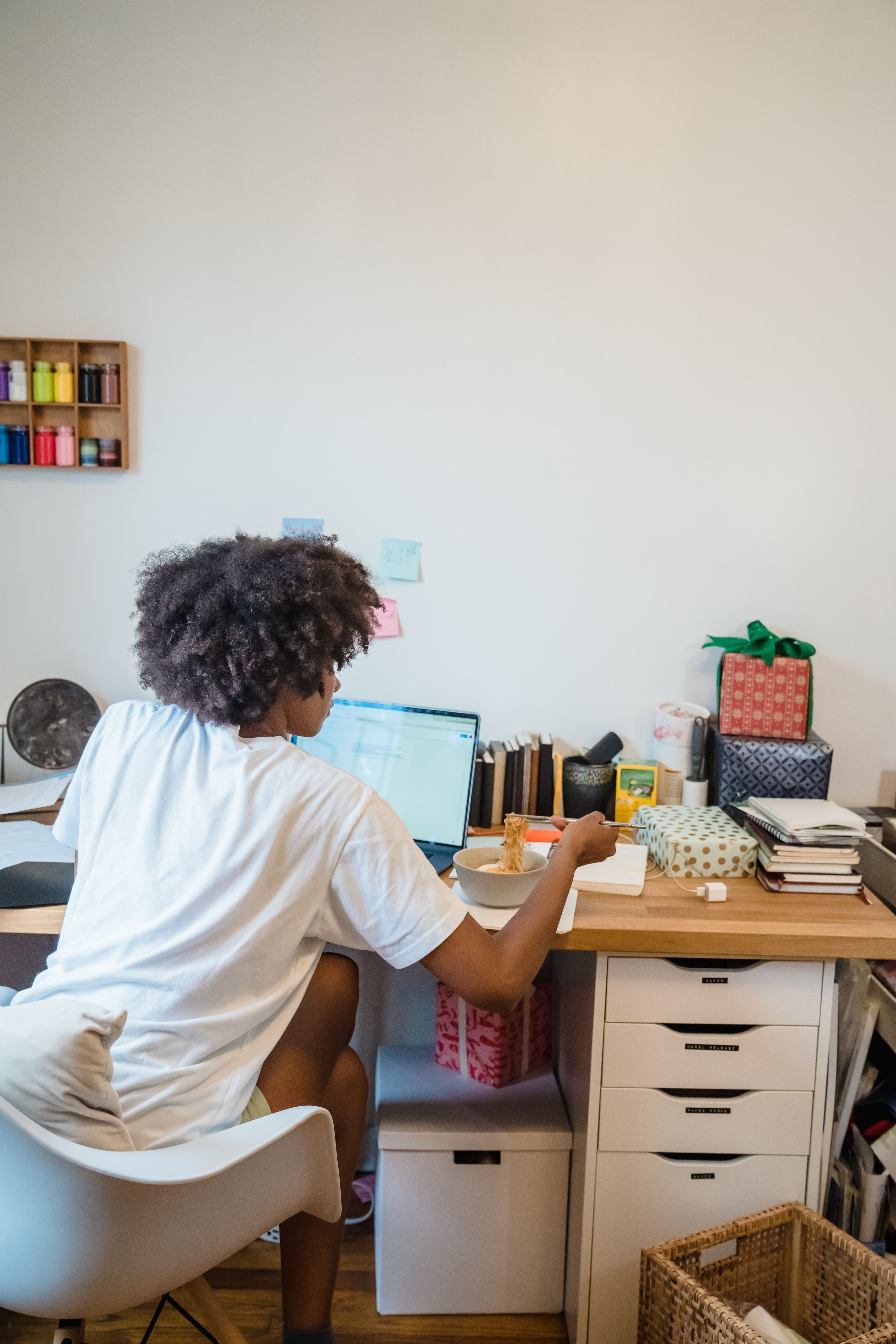 Student at a desk with a laptop, sticky notes, and art supplies on the wall